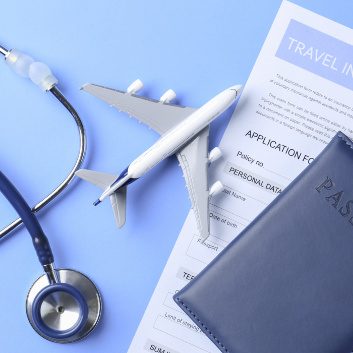 Fonendoscopi, avió en miniatura, passaport i document d’assegurança de viatge sobre una superfície blava.