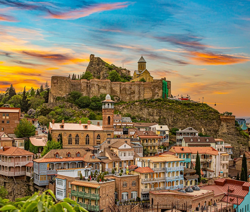 Vista panoràmica d’una ciutat històrica del Caucas amb cases tradicionals, esglésies i una fortalesa al cim d’un turó, il·luminada pel capvespre.